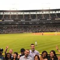 a wide shot of the stadium with everyone who came to the event crowded together at the home run fence while the game is going on in the background.